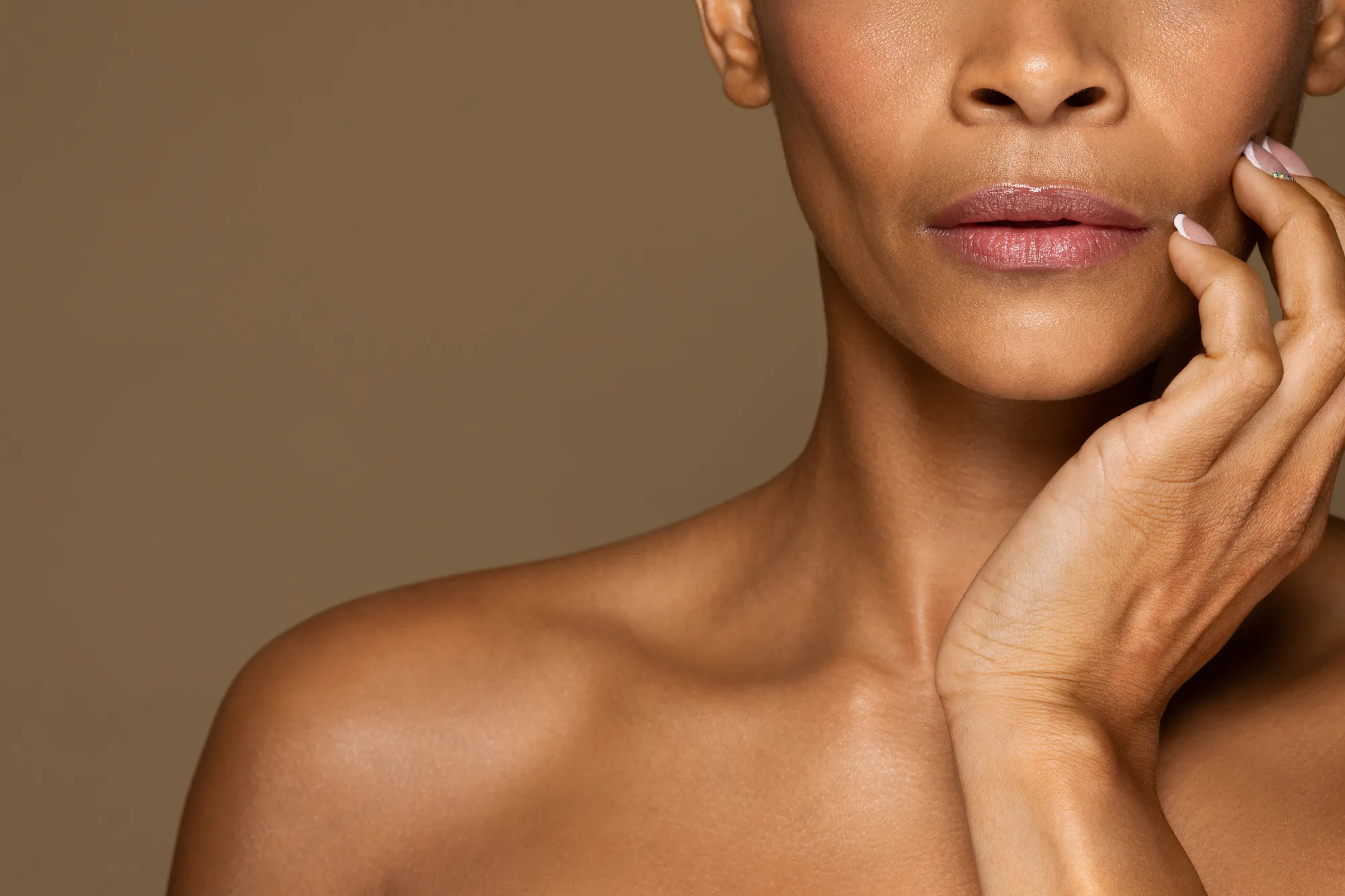 A woman touching her cheek with a calm expression, bare shoulder visible in soft light